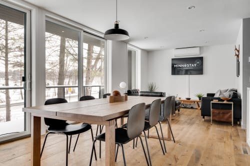 Modern dining area with a rustic table and sleek black chairs, overlooking a winter landscape.