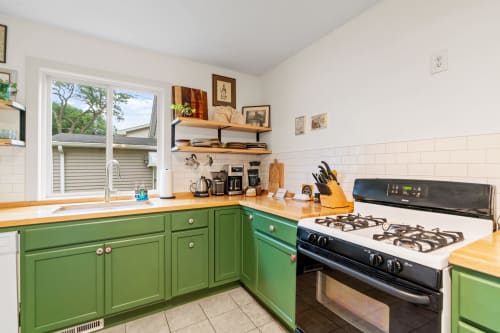 A cozy kitchen with green cabinets and a large window providing natural light.