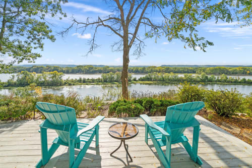 A tranquil riverside view featuring turquoise Adirondack chairs and autumn foliage.