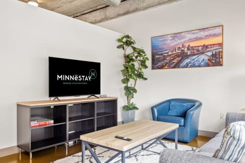 A modern living room featuring MINNESTAY branding and a vibrant city skyline painting.