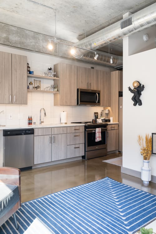 A stylish, modern kitchen featuring light wood cabinets and sleek appliances, accented by a bold blue striped rug.