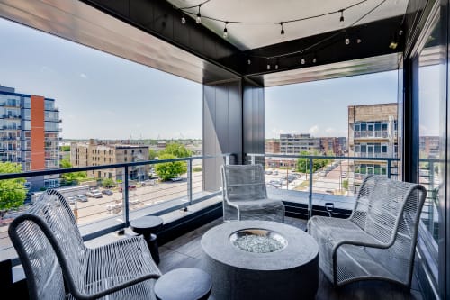 A modern balcony featuring woven chairs and a stylish fire pit with city views.