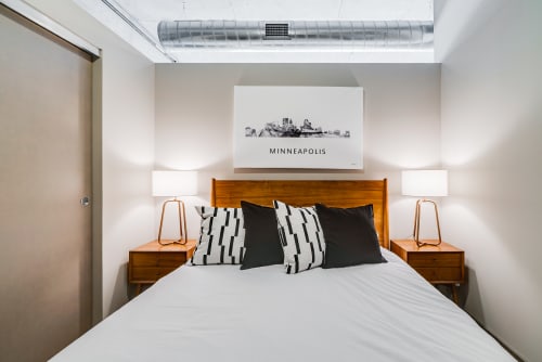 A modern bedroom featuring a minimalist design with a bed, stylish pillows, and a skyline artwork.