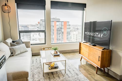 Modern living room featuring a city view, stylish furniture, and a TV displaying 'MINNESTAY'.