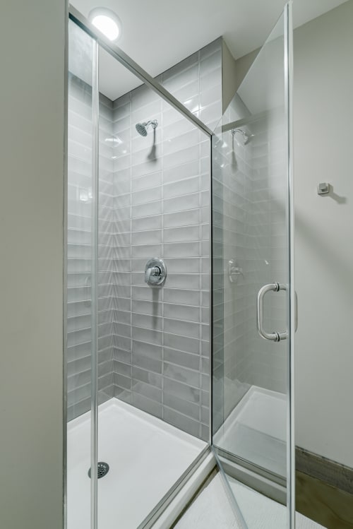 A modern shower enclosure with gray tiled walls and clear glass doors.