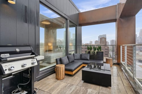 Stylish urban balcony with a grill and cozy seating overlooking the city skyline.