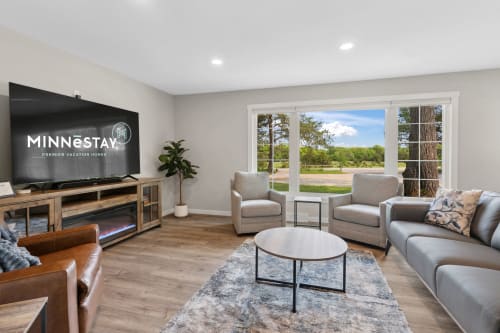 A bright and modern living room featuring a large TV, cozy seating, and scenic views.