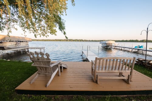 A tranquil lakeside view with rustic seating and boats in the background.