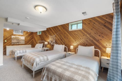 A cozy bedroom with three beds, wooden paneling, and soft lighting.