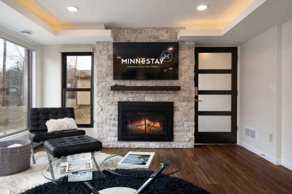 Modern living room with black lounge chair, glass coffee table, fireplace, and flat-screen TV.