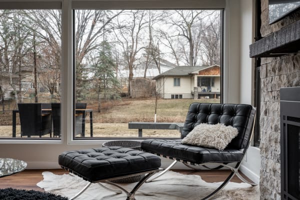 Interior view featuring a black lounge chair and ottoman overlooking a serene outdoor scene.