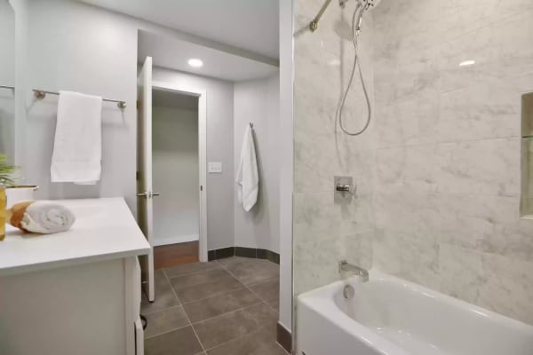 Clean modern bathroom with marble tiles, a bathtub, and neatly arranged towels.