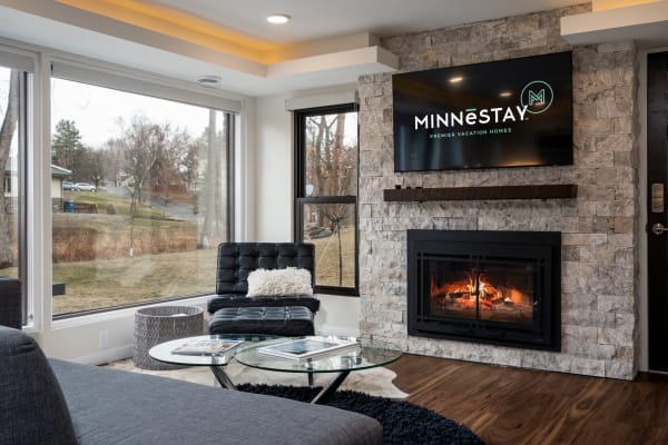 Modern living room with large windows, fireplace, and MINNESTAY TV display.