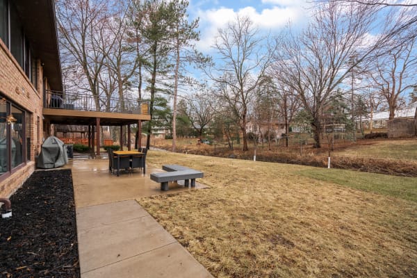 Backyard of a modern home showcasing a stone patio, wicker dining set, and trees.