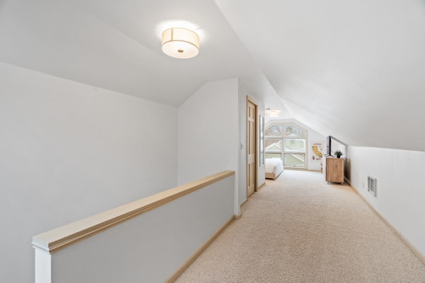 Spacious upper hallway with sloped ceiling, light carpet, and wooden furnishings.