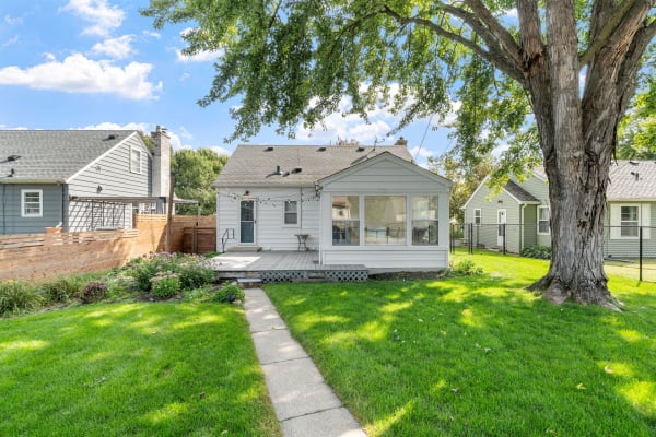 A quaint house with a wooden deck, surrounded by green grass and colorful flowers under a blue sky.