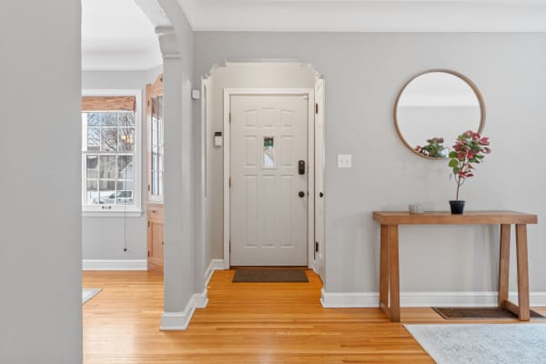 An entryway with a white door, wooden console table, mirror, and hardwood floor.