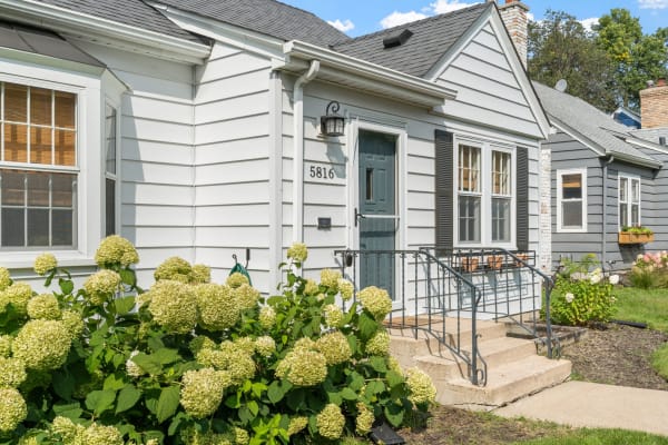 A single-story house with gray siding, blue front door, and hydrangea flowers at the entrance.