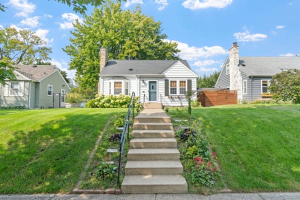 A single-story house with white siding, blue door, and lush green lawn surrounded by flowers.