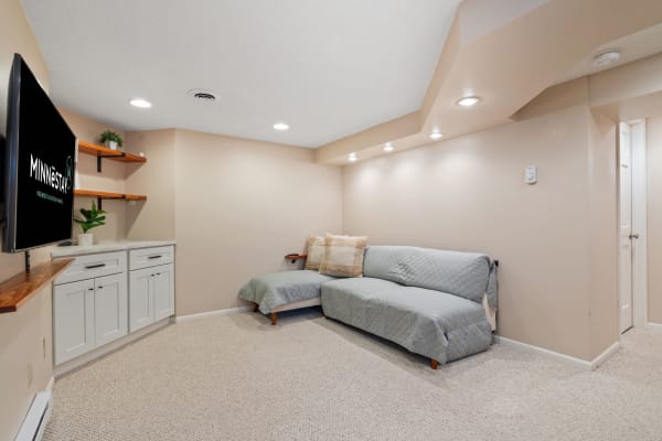 Cozy basement living room featuring a light gray sectional couch and a flat-screen TV on the wall.