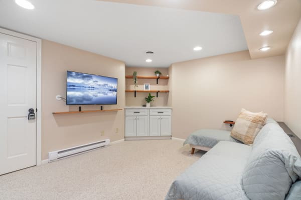 Cozy basement living area with beige walls, a wall-mounted TV, and a gray sofa.