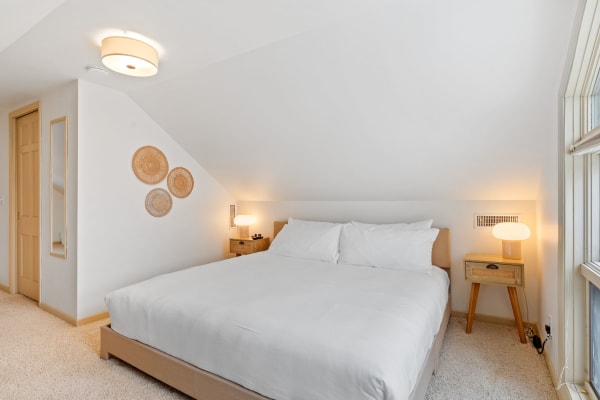 Minimalist bedroom with a layered bed, woven wall art, and a stylish lamp.