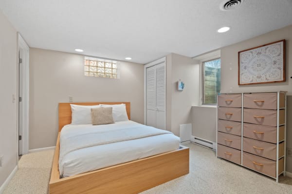 A cozy bedroom featuring a wooden bed, beige walls, and a dresser with fabric drawers.