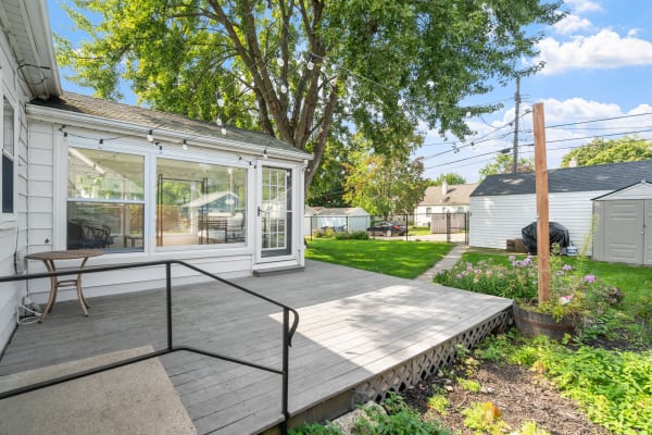 A backyard featuring a wooden deck, sunroom, and colorful flower beds.