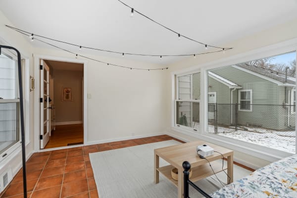 Cozy sunroom with string lights and terracotta floor, featuring a projector and snowy outdoor view.