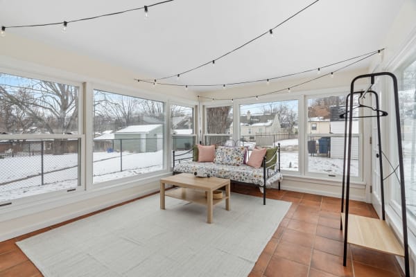Sunroom with large windows, a floral daybed, decorative lights, and snow outside.