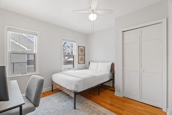 Minimalist bedroom with a bed, desk, and natural light from windows.