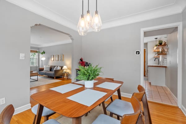 A modern dining space with a wooden table, fern centerpiece, and a view into a cozy living room and kitchen.