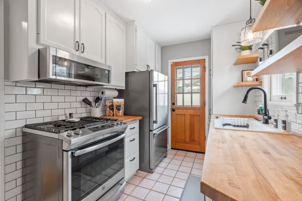 A bright kitchen featuring stainless steel appliances, white cabinets, and wooden shelves.