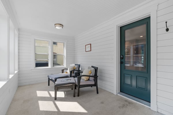 A sunroom with white walls, wicker chairs, and a teal door.
