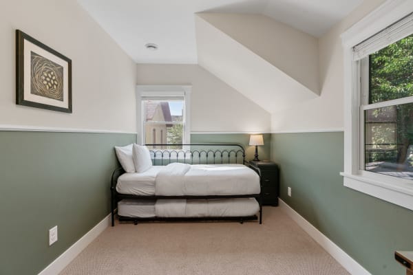 Cozy bedroom featuring a black iron bed, sage green wall, and a sloped ceiling.