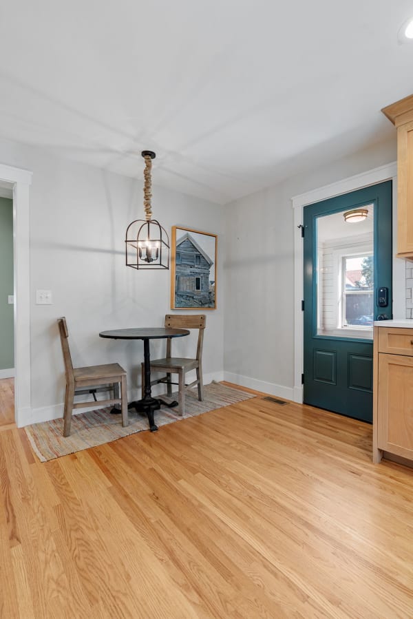 A small wooden table and chairs in a cozy dining nook with a green door and pendant light.