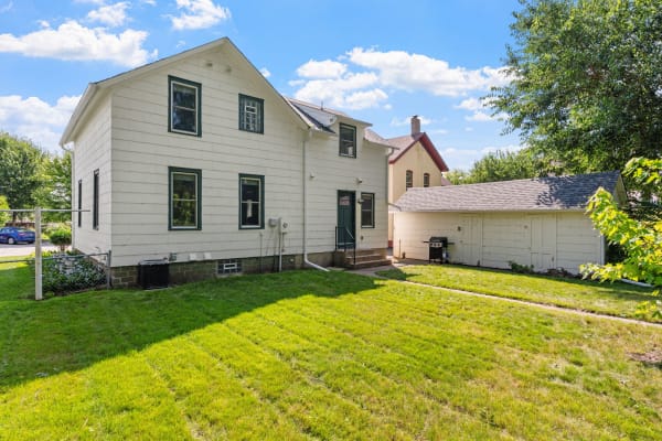 Exterior view of a two-story white house with green trim, lawn, and a white shed.