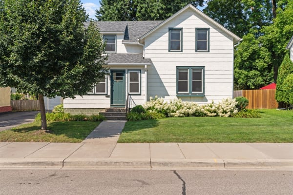 A two-story house with white siding, green trim, and a front lawn adorned with flowers.