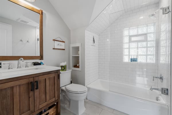 Modern bathroom with wooden vanity, white tiles, and glass shower.