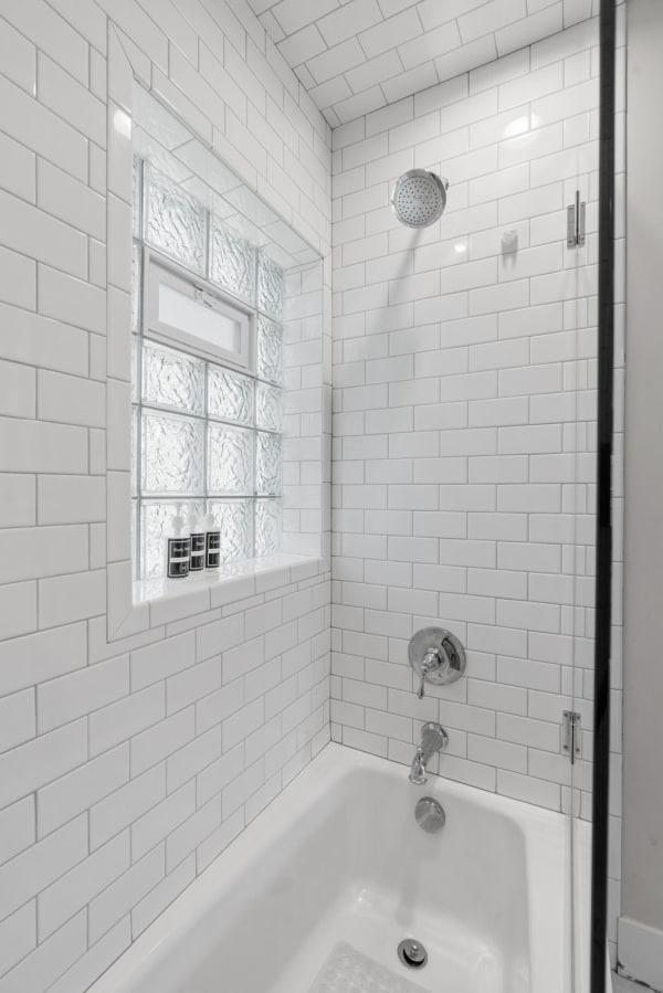 Modern shower space featuring white tiles and a glass block window.