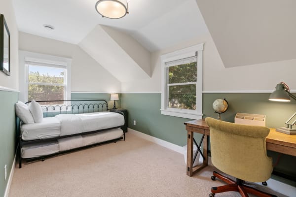 Cozy bedroom with a daybed and wooden desk under a sloped ceiling.