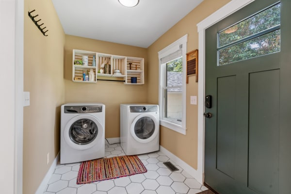 Bright laundry room featuring white washing machines, wooden shelving, and a dark green door.