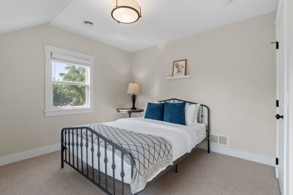 A modern bedroom featuring a black metal bed, blue pillows, and a lamp by the window.