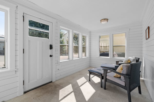 Sunroom with a white door, large windows, and cozy seating arrangement.