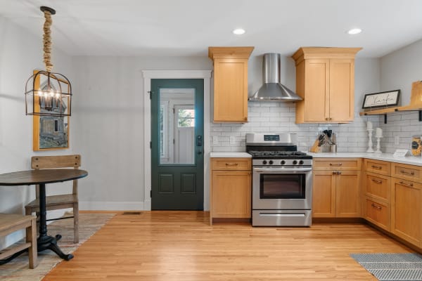 Modern kitchen featuring light wood cabinets, stainless steel appliances, and a round table with chairs.