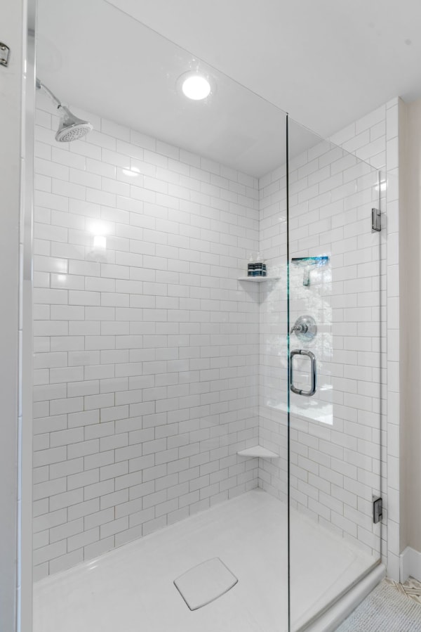 A contemporary walk-in shower featuring white subway tiles, glass doors, and a built-in shelf for toiletries.