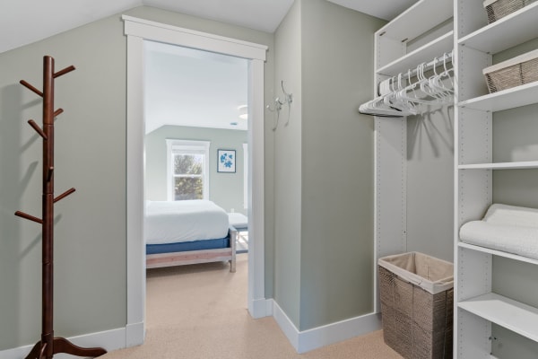 Interior view of a storage area with coat rack, shelves, and visible bedroom beyond.