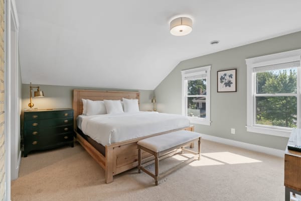 A cozy bedroom with a wooden bed, green dresser, and natural light from windows.