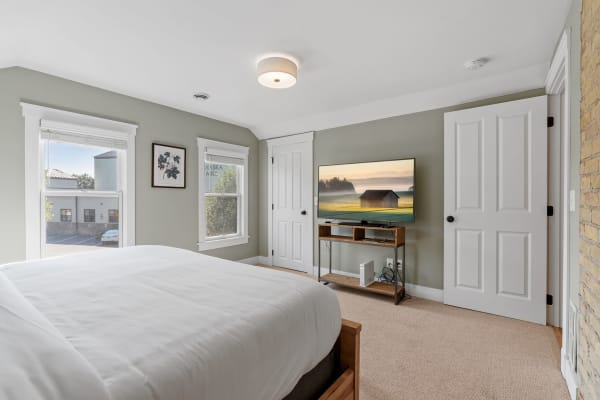 A cozy bedroom featuring a bed, windows, a TV, and a wooden media console.