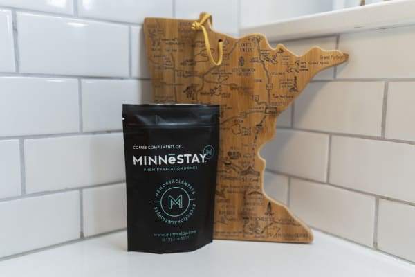 Black coffee bag next to a wooden cutting board shaped like Minnesota on a white countertop.